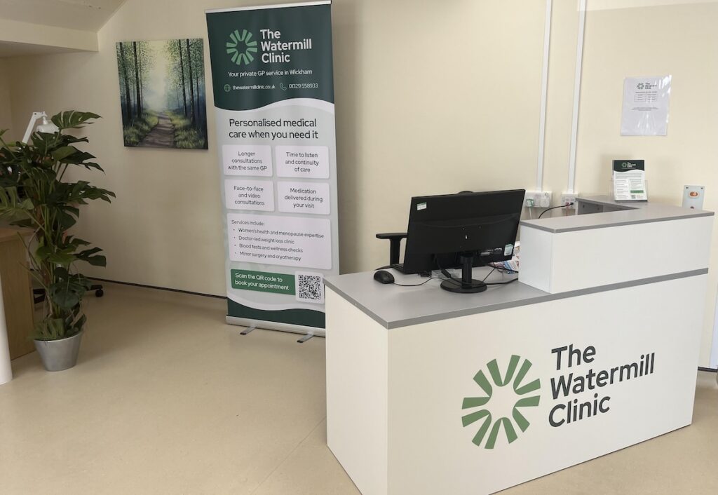 The bright, welcoming reception area at The Watermill Clinic in Wickham, featuring the clinic's branded desk and a banner highlighting personalised private GP services.